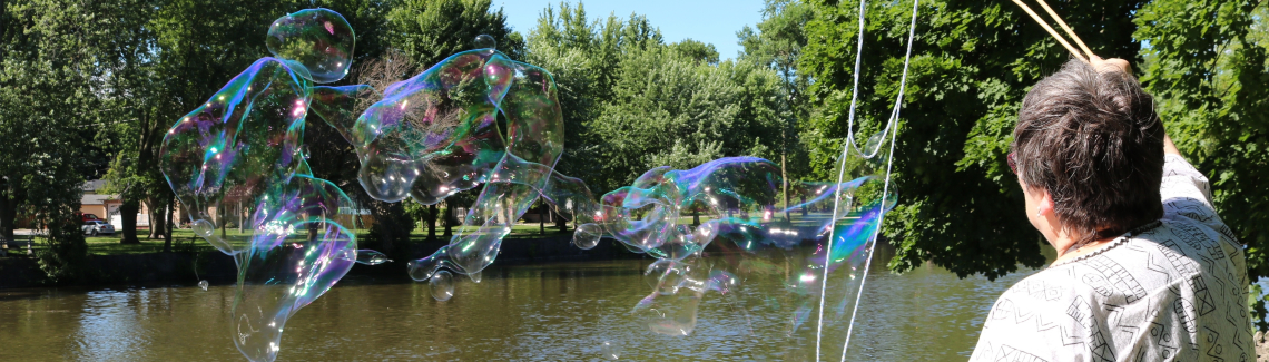 Harcourt congregant, Lynn Hancock, using two wands to blow big bubbles by the Speed River that flows through Guelph