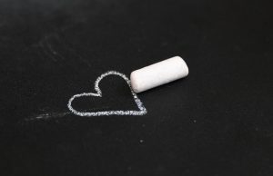 White heart drawn in chalk on black pavement with a white stick of chalk laying beside the heart