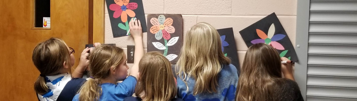 Girl Guides doing crafts of flowers and holding them against the wall in a group with their backs turned to the camera
